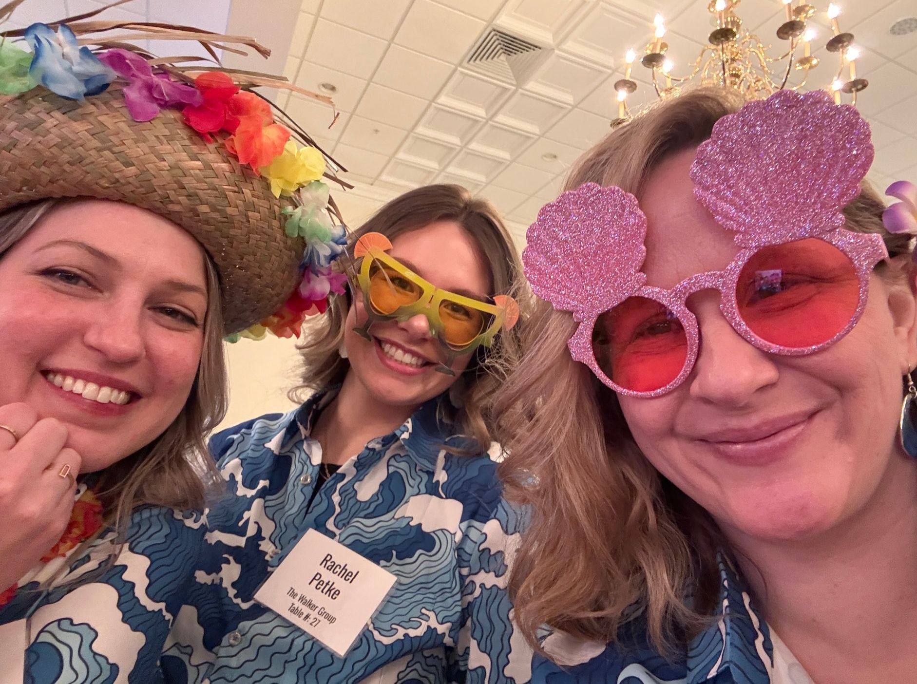 Diana, Rachel, Kristen smiling, wearing Hawaiian shirts and novelty glasses, at an indoor event.