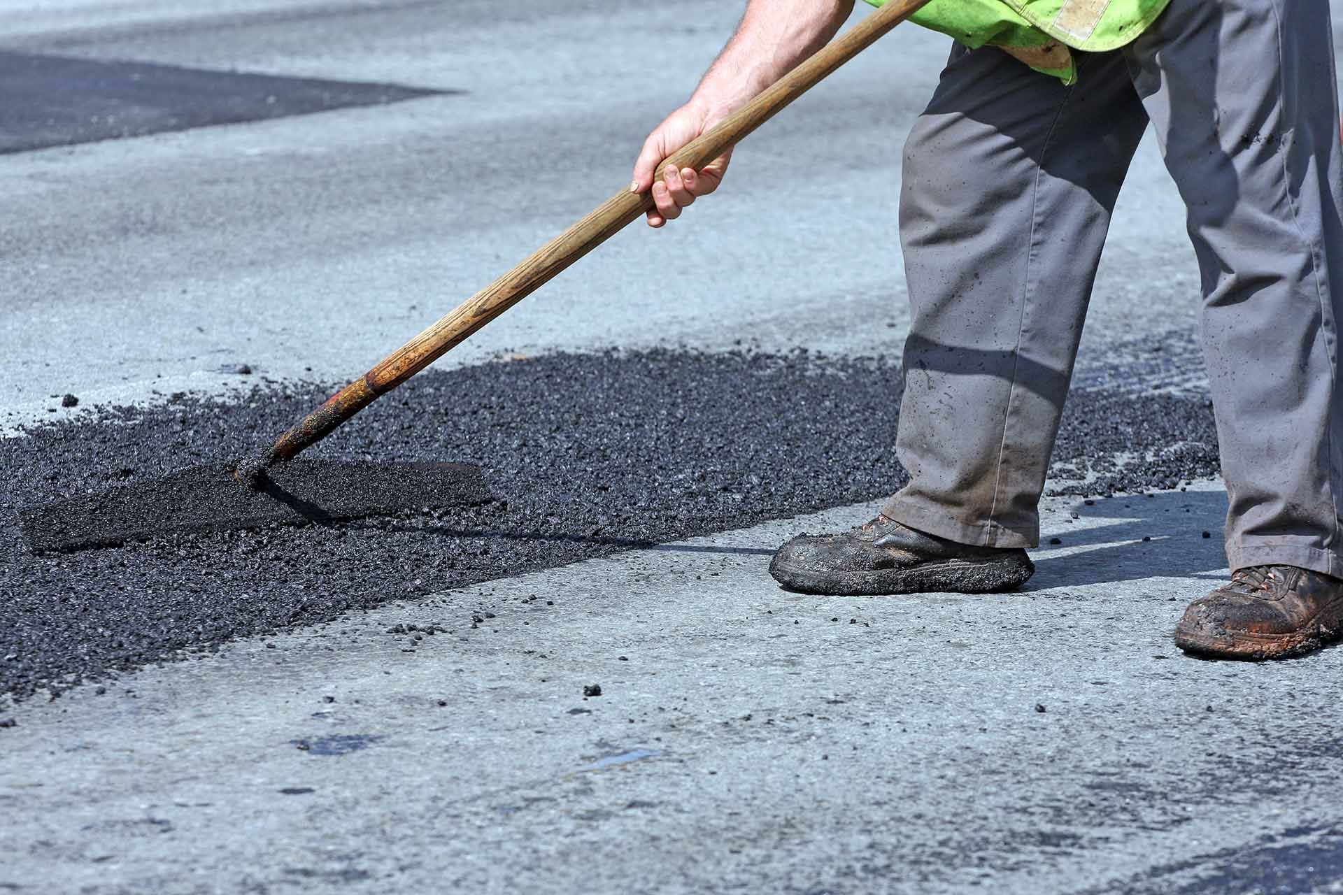 A man is spreading asphalt on the ground with a rake — Memphis, TN — Davis Pavement