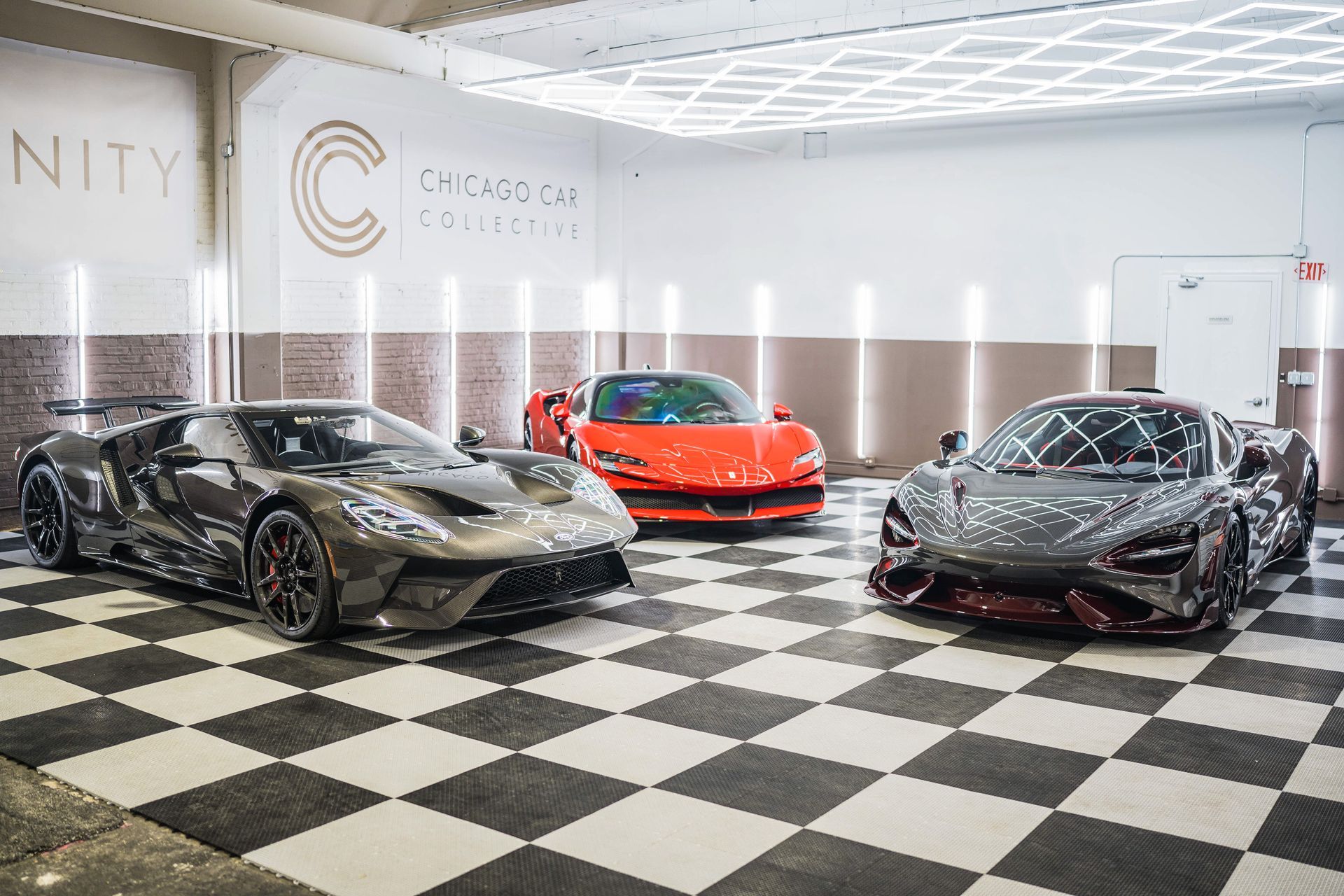 Three luxury sports cars on a checkered floor in a showroom: grey Ford, red Ferrari, and grey McLaren.