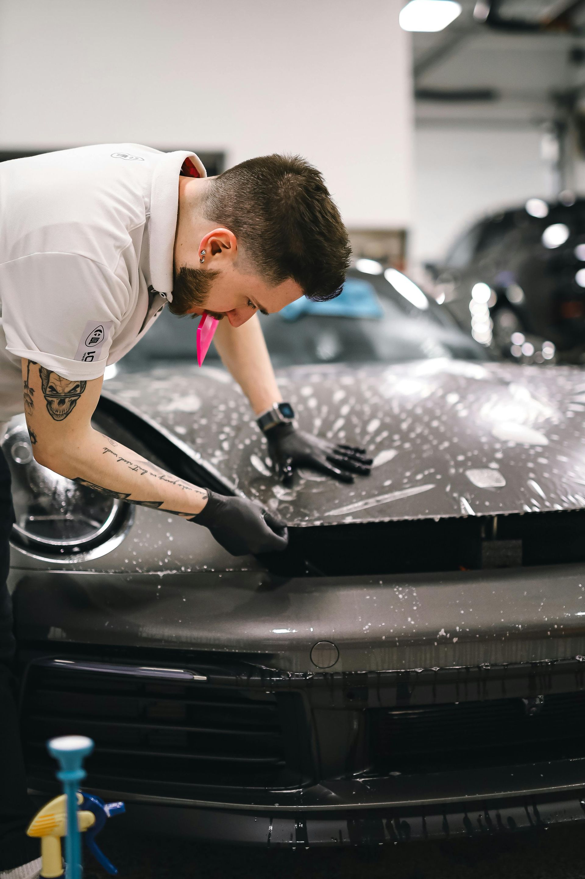 Person applying film to the hood of a dark car, using a squeegee in a workshop.