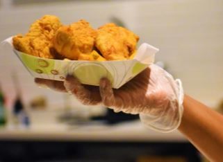 Una persona que lleva guantes sostiene un plato de pollo frito.