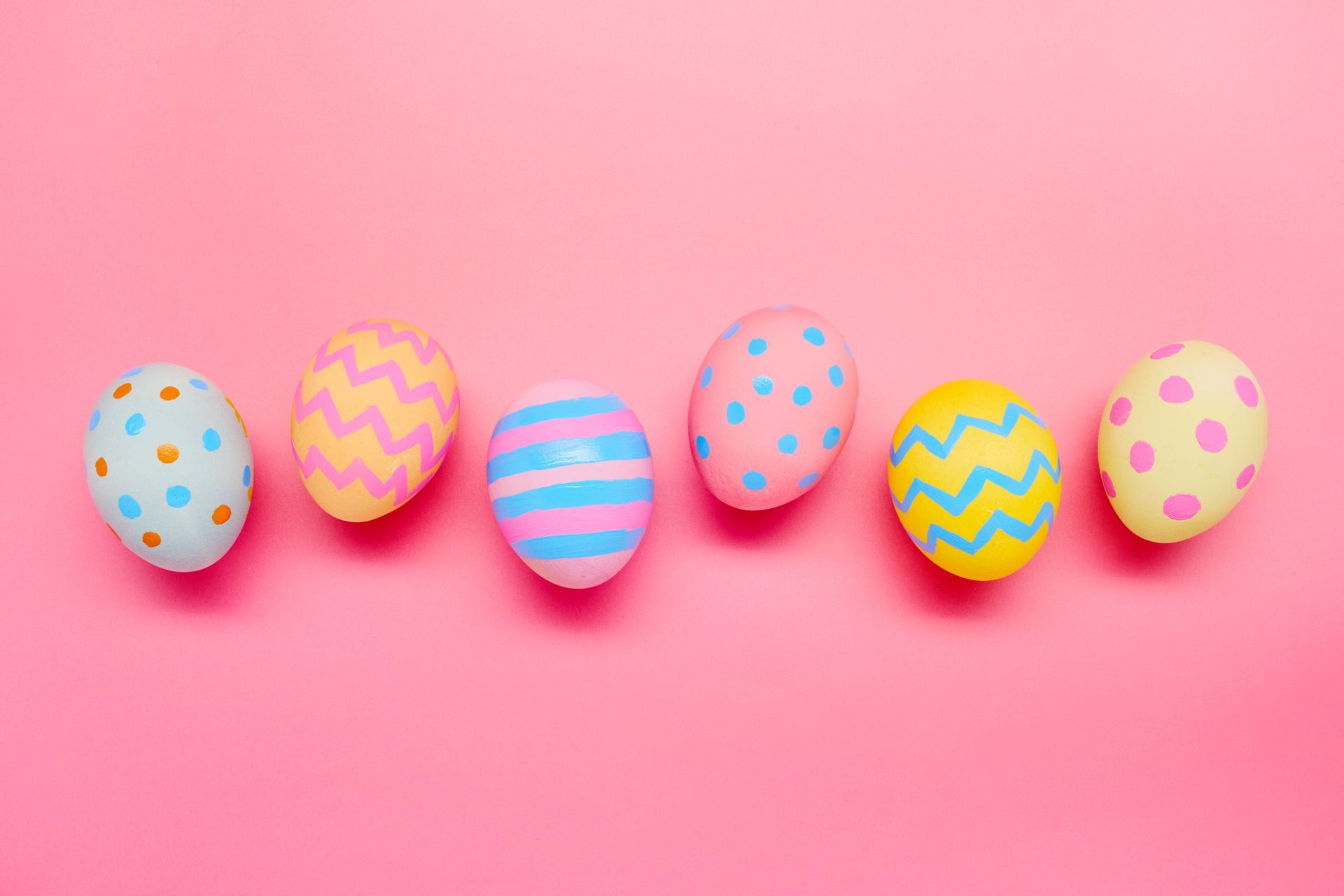Six pastel Easter eggs in a row on a pink background; each has a different colorful pattern.