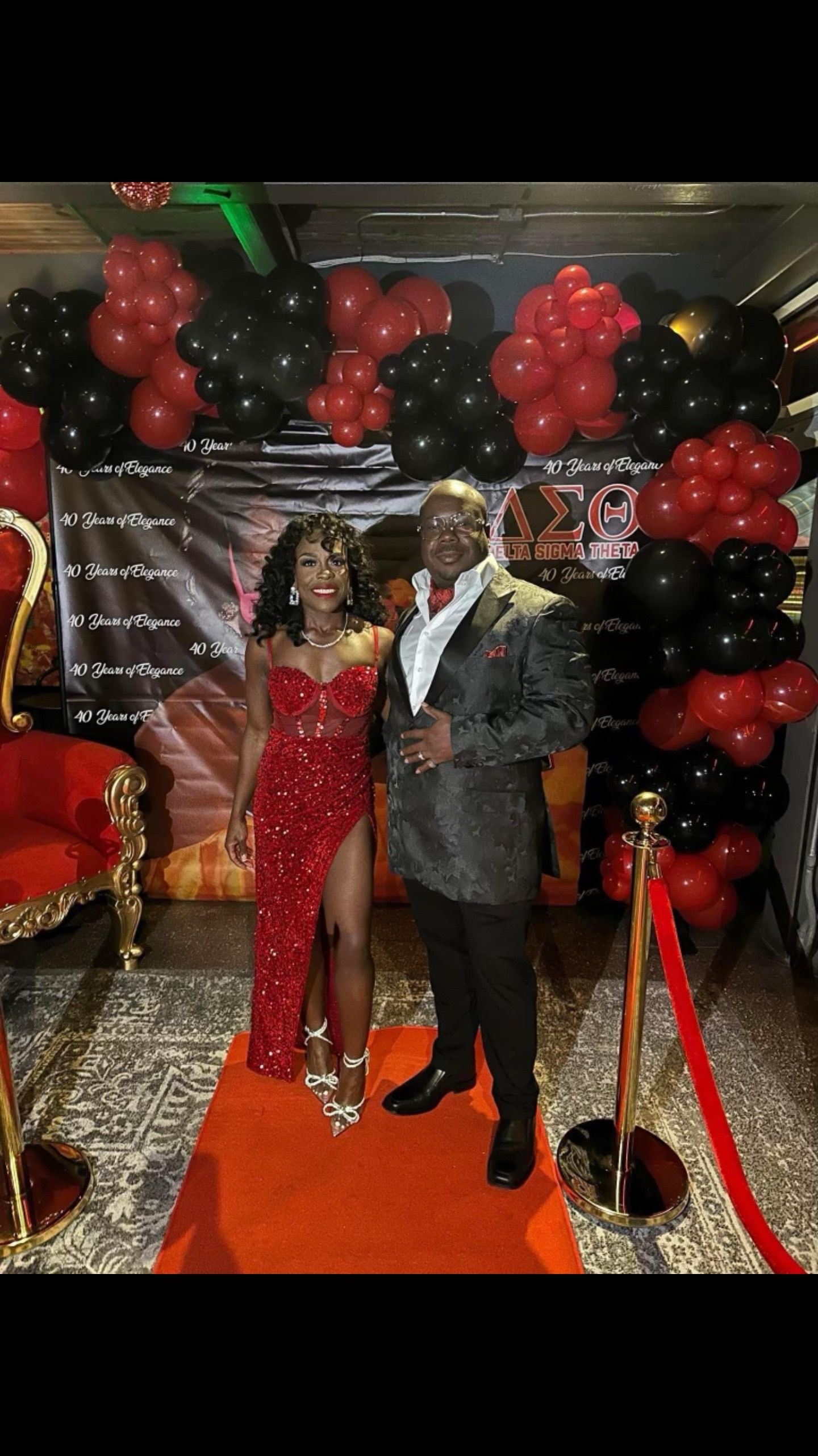 A man and a woman are standing on a red carpet at a party.