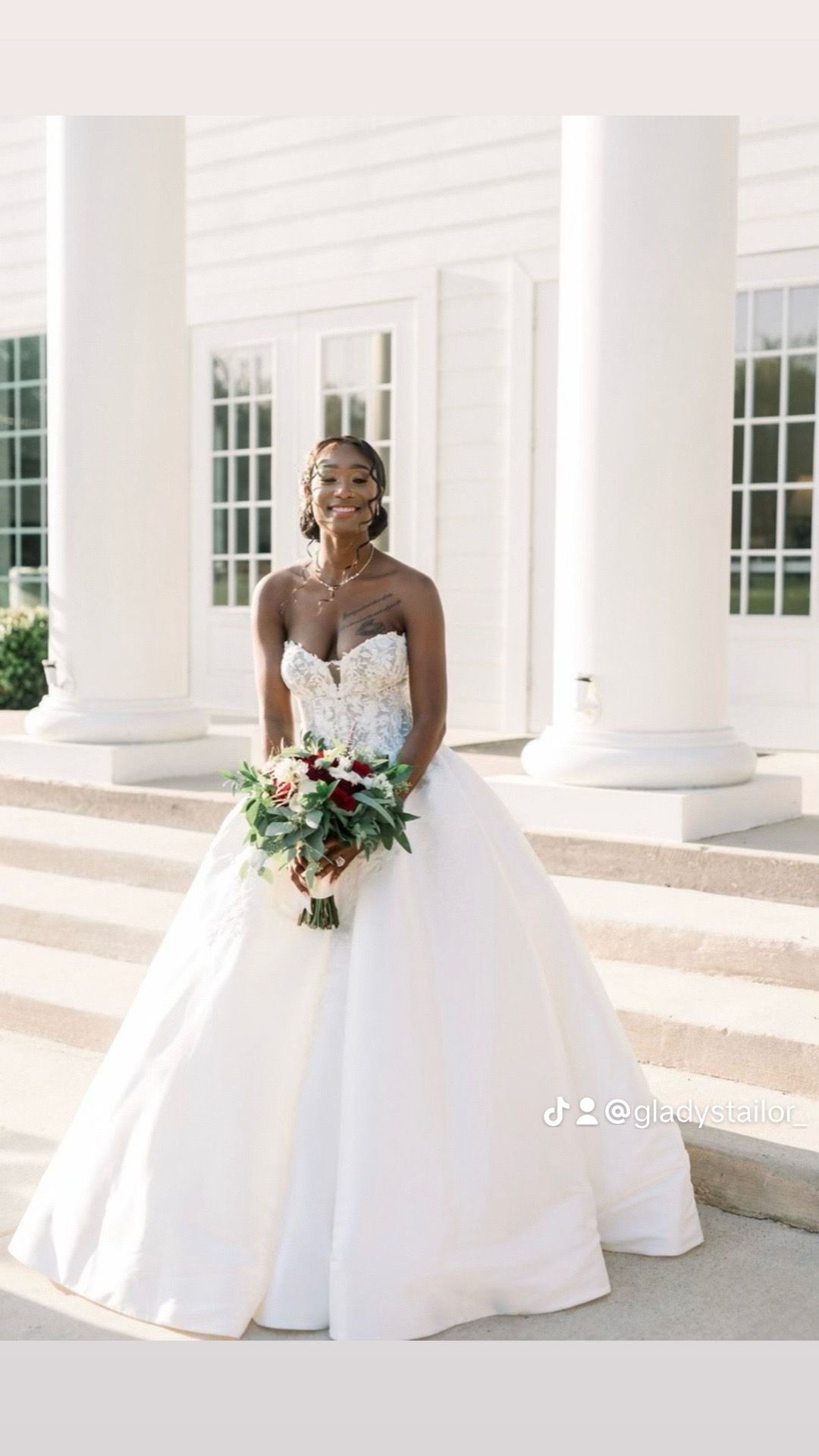 A bride in a wedding dress is standing in front of a white building holding a bouquet of flowers.