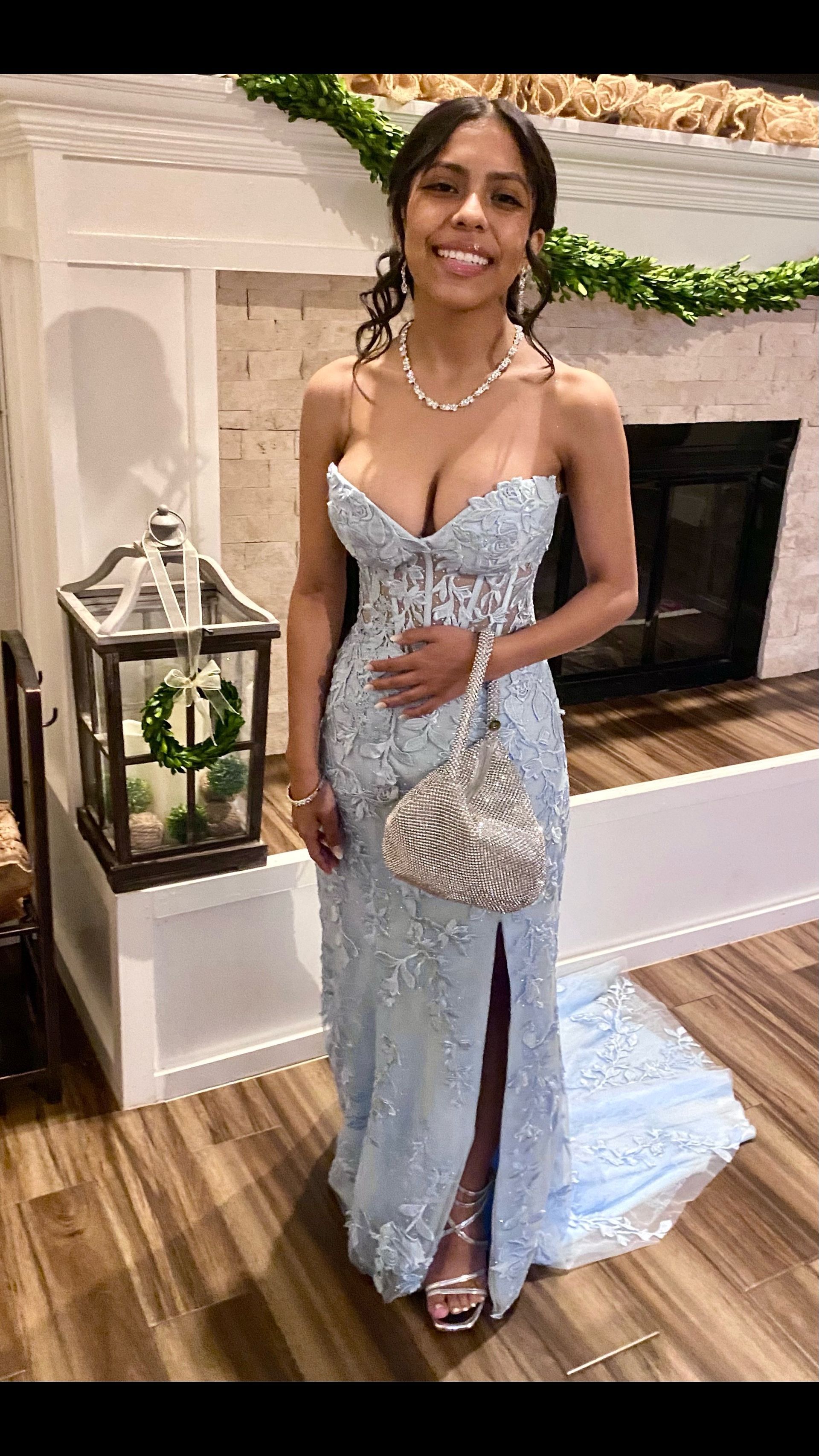 A woman in a light blue dress is standing in front of a fireplace.