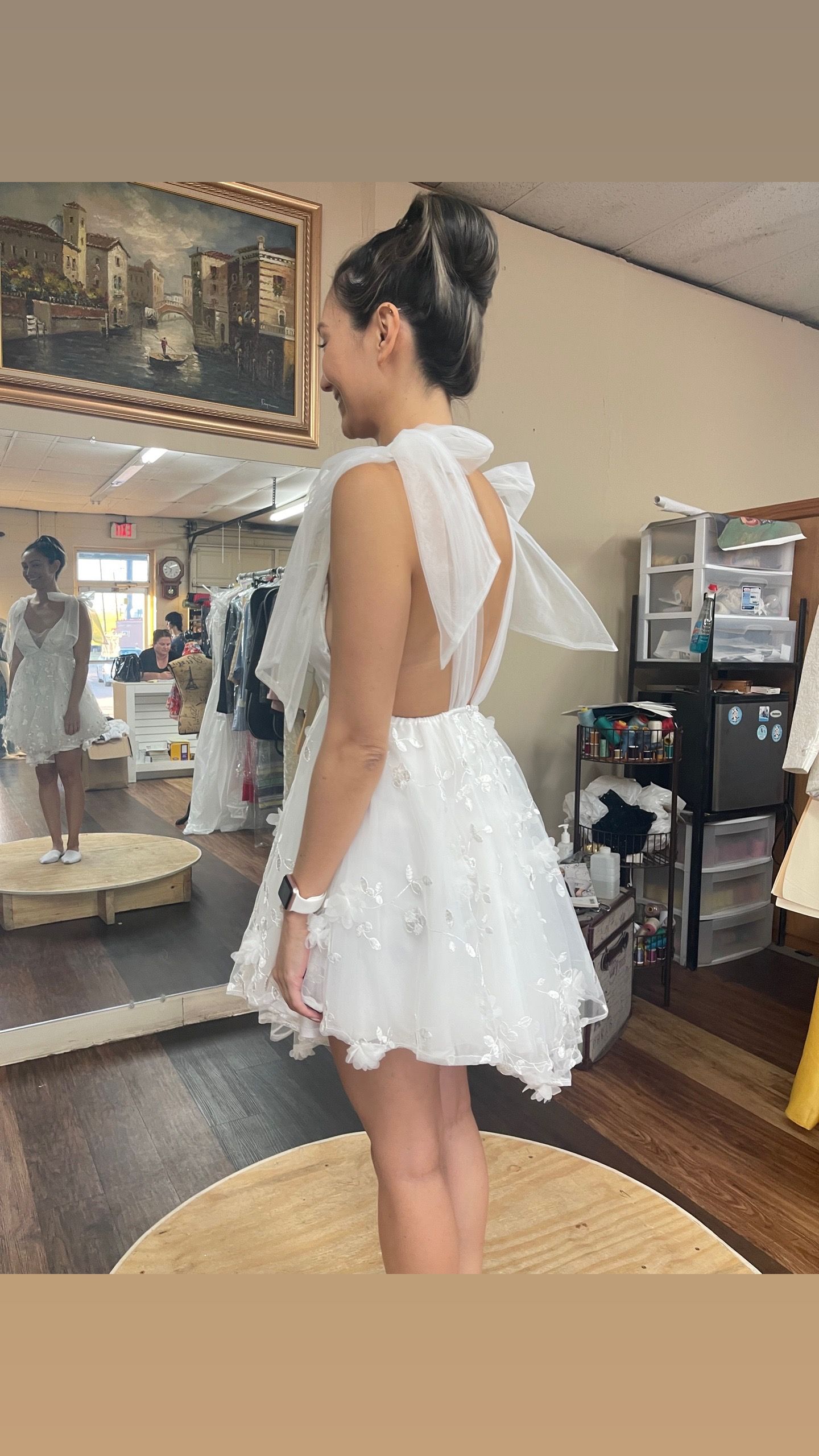 A woman in a white dress is standing in front of a mirror.