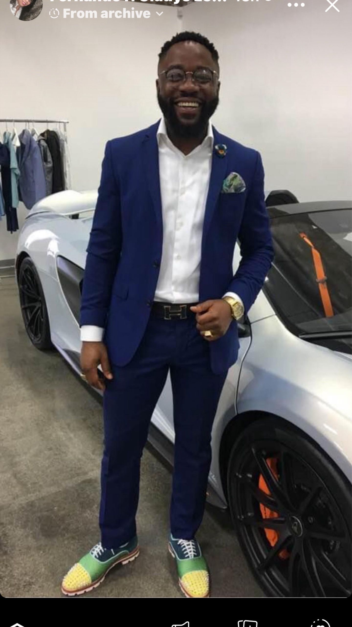 A man in a blue suit is standing in front of a silver sports car.