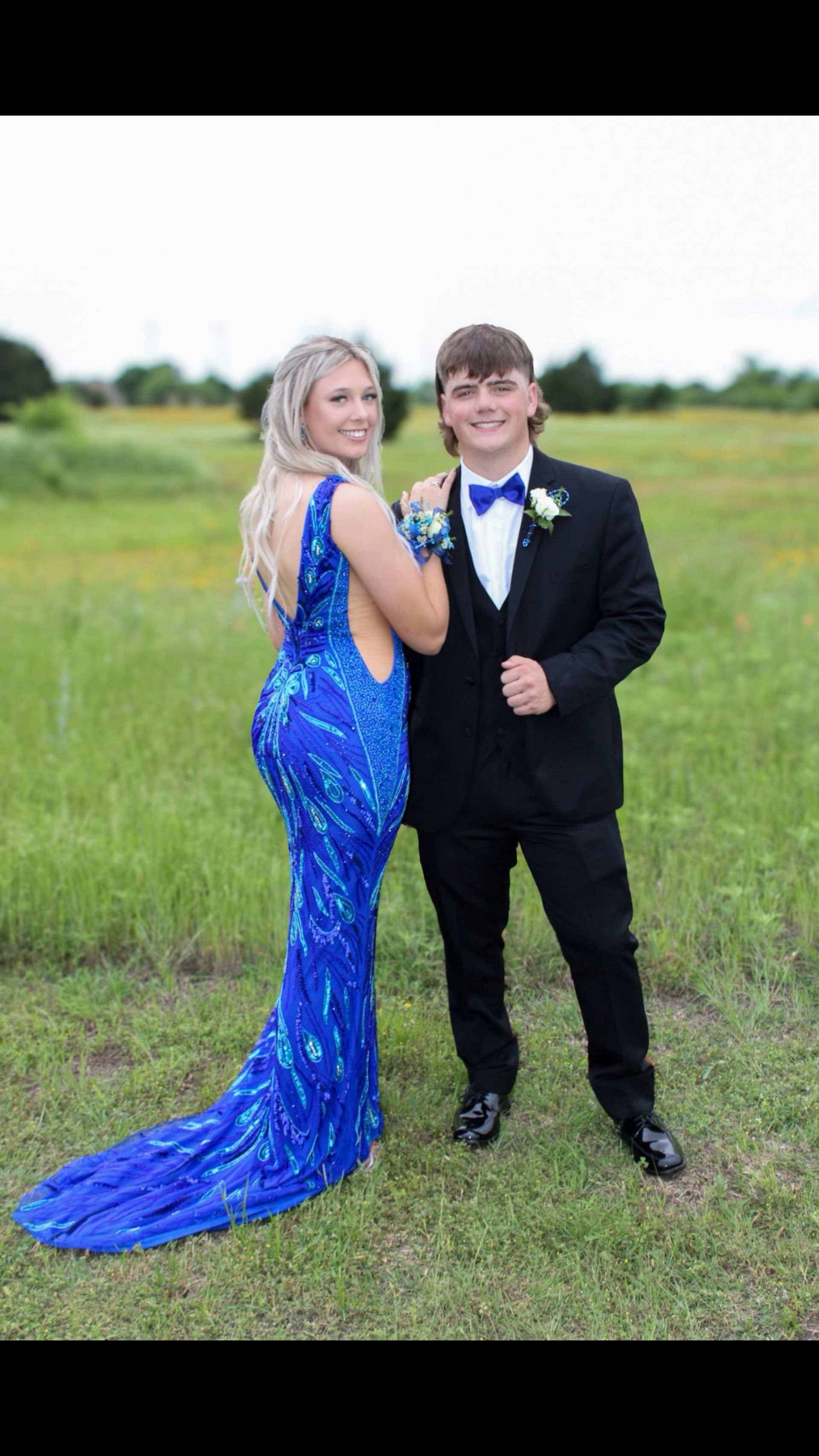 A man and a woman are posing for a picture in a field . the woman is wearing a blue dress.