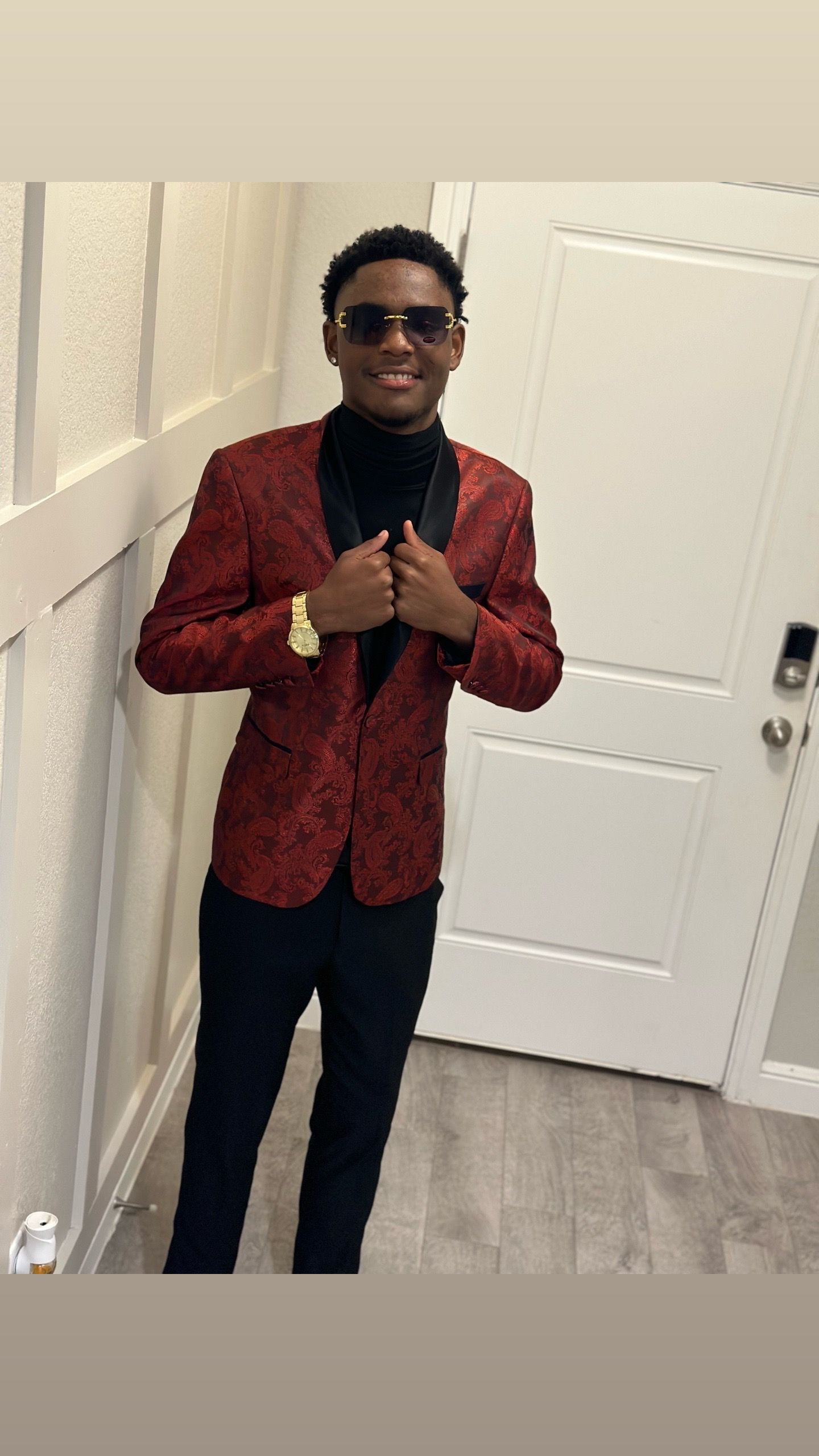 A man wearing a red tuxedo jacket and black pants is standing in front of a door.