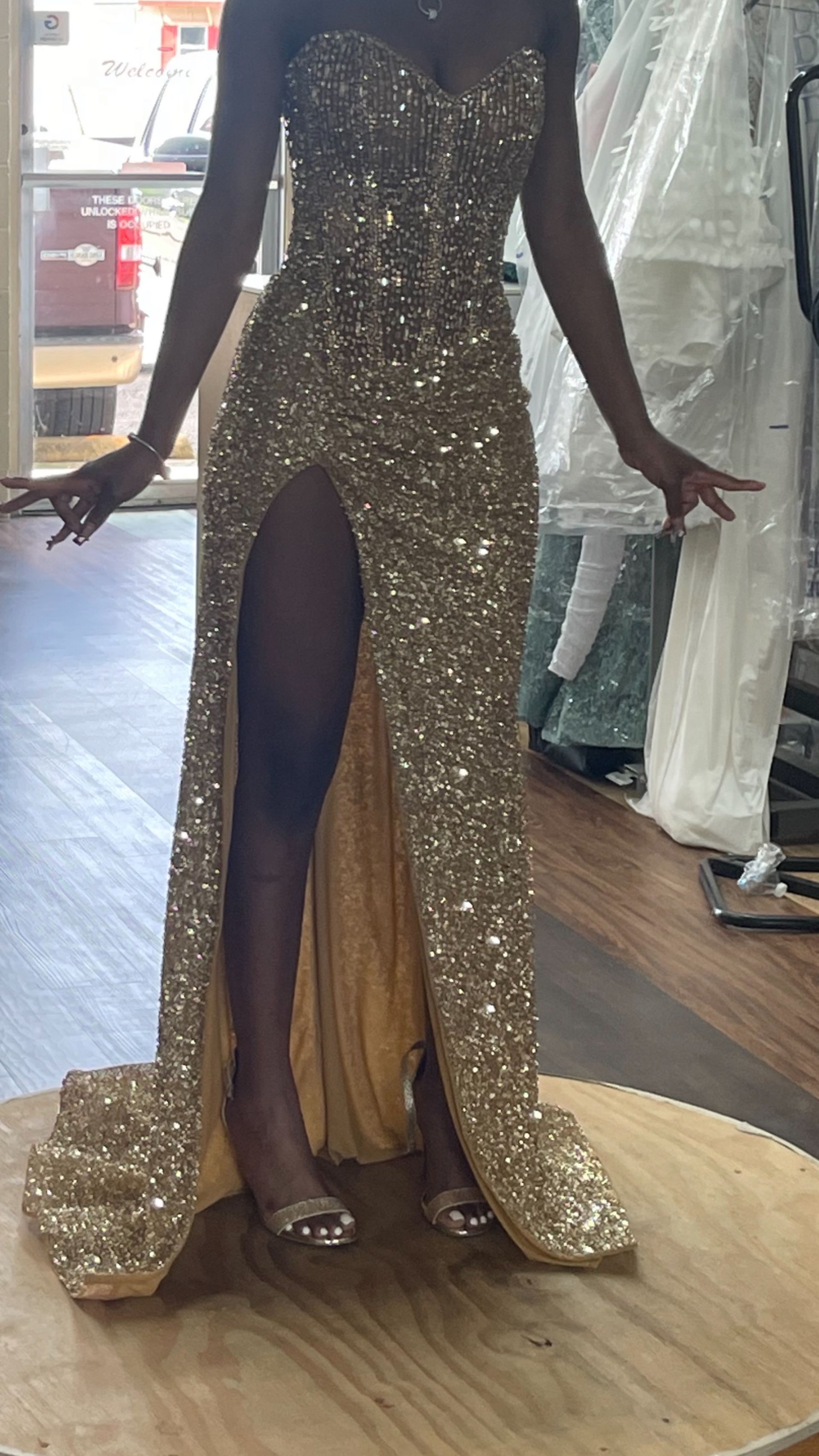 A woman is wearing a gold sequined dress with a high slit.