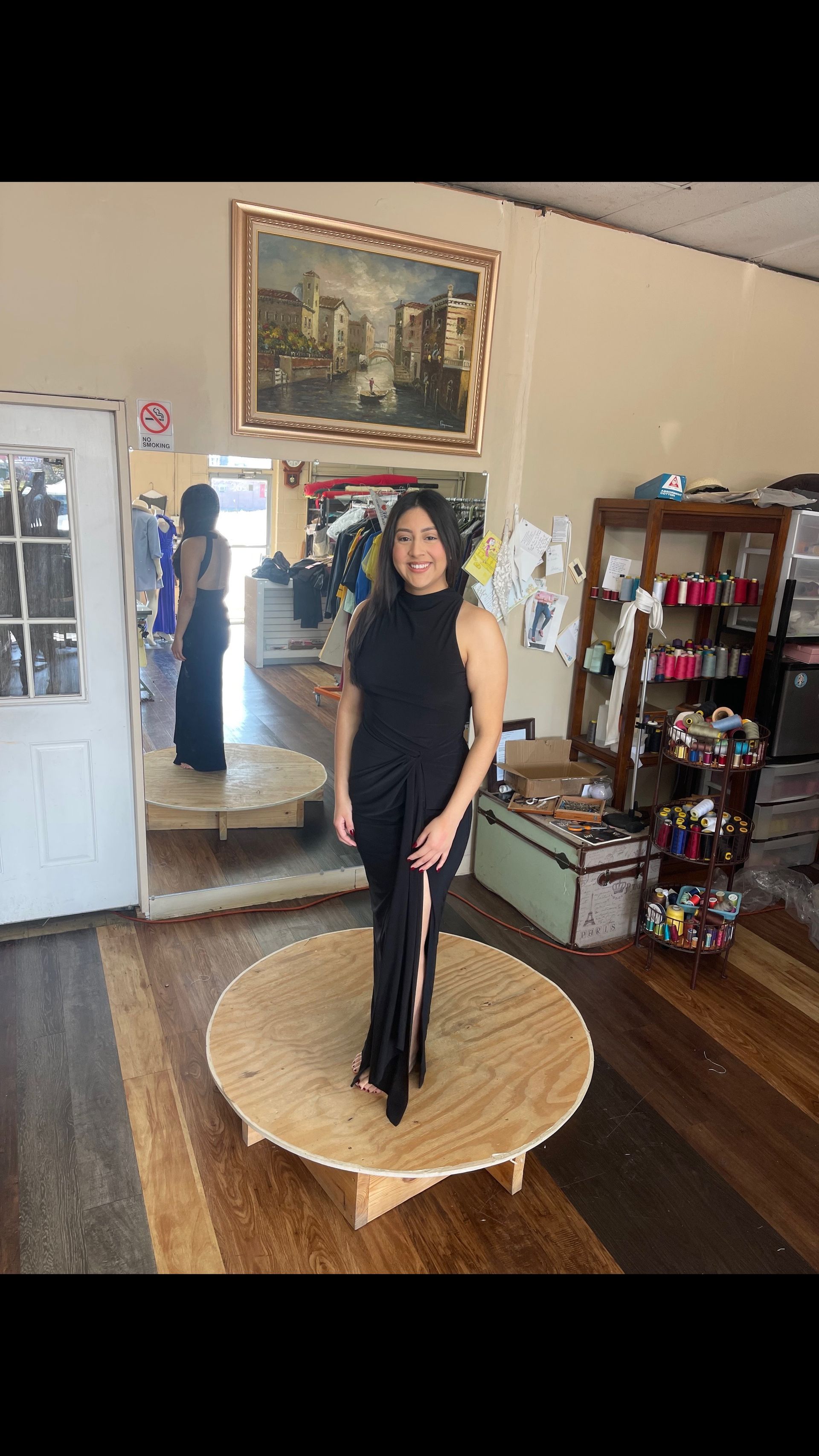 A woman in a black dress is standing on a wooden table in a room.
