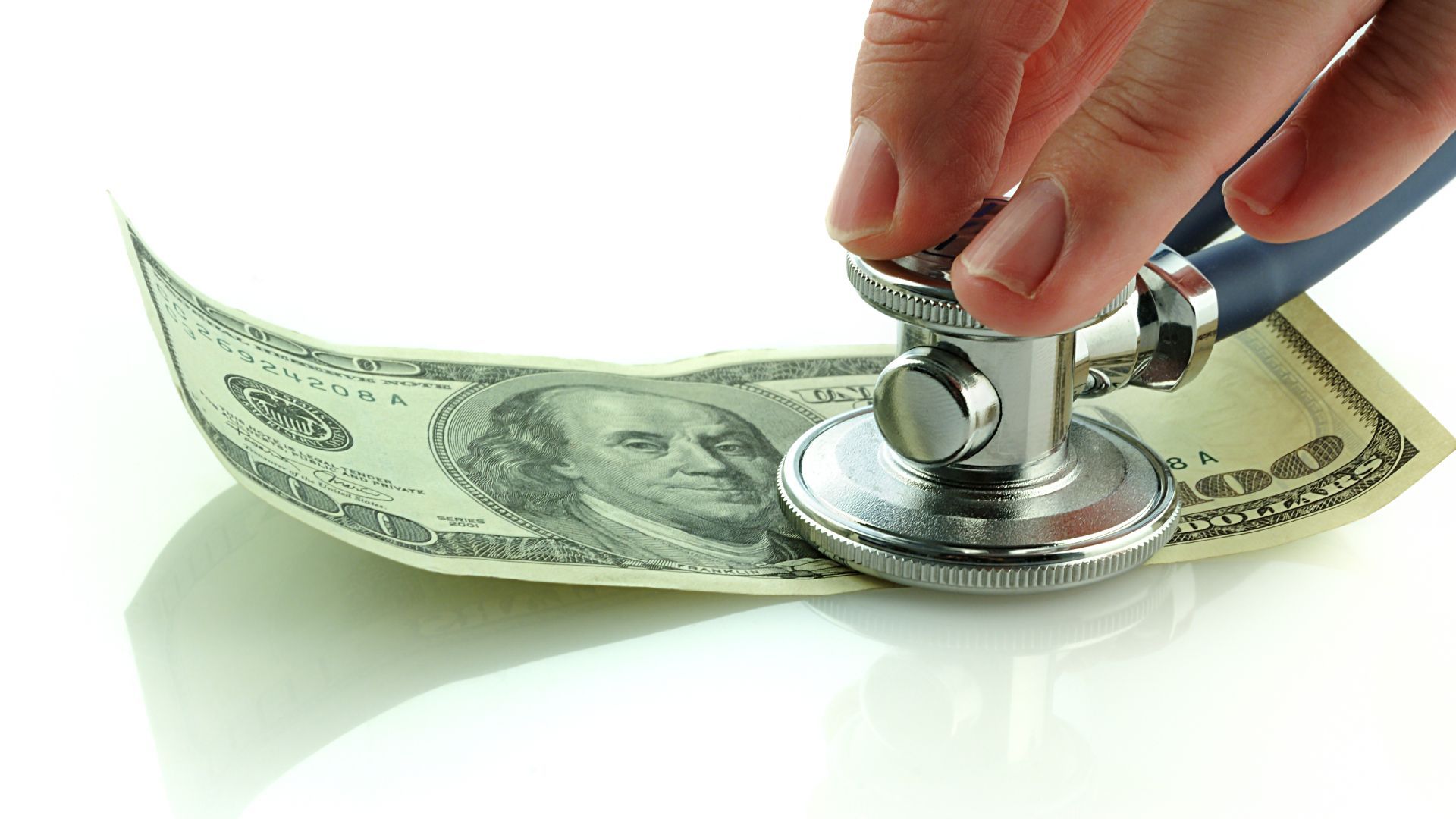 A person is holding a stethoscope over a dollar bill