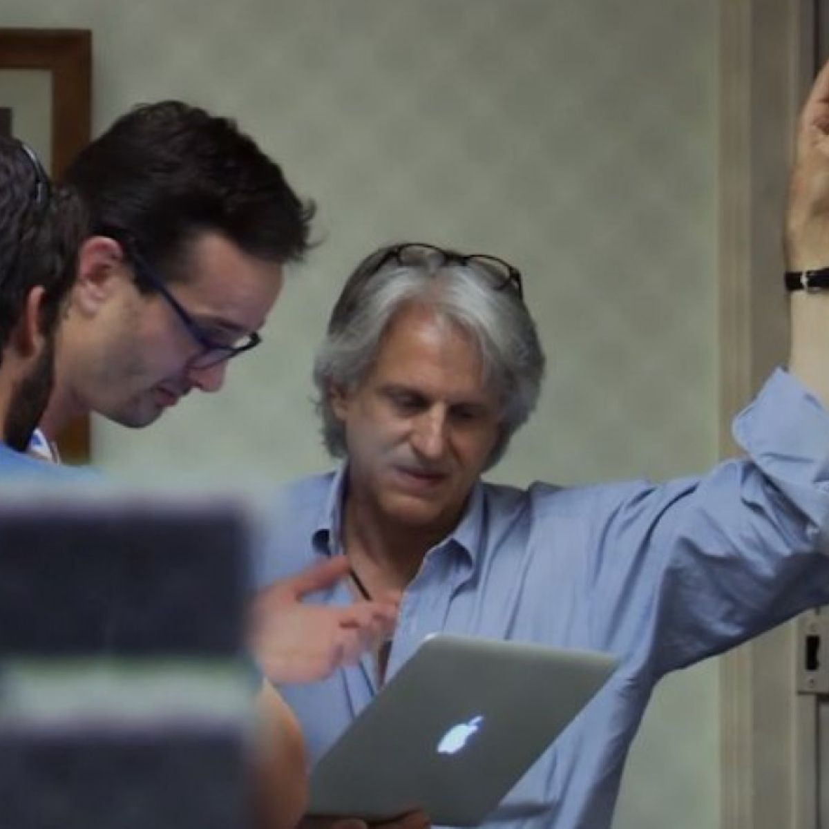 A group of men are looking at an apple laptop