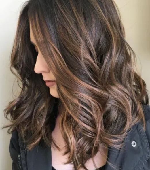 Woman getting hair washed at a salon; stylist holds showerhead over her head.