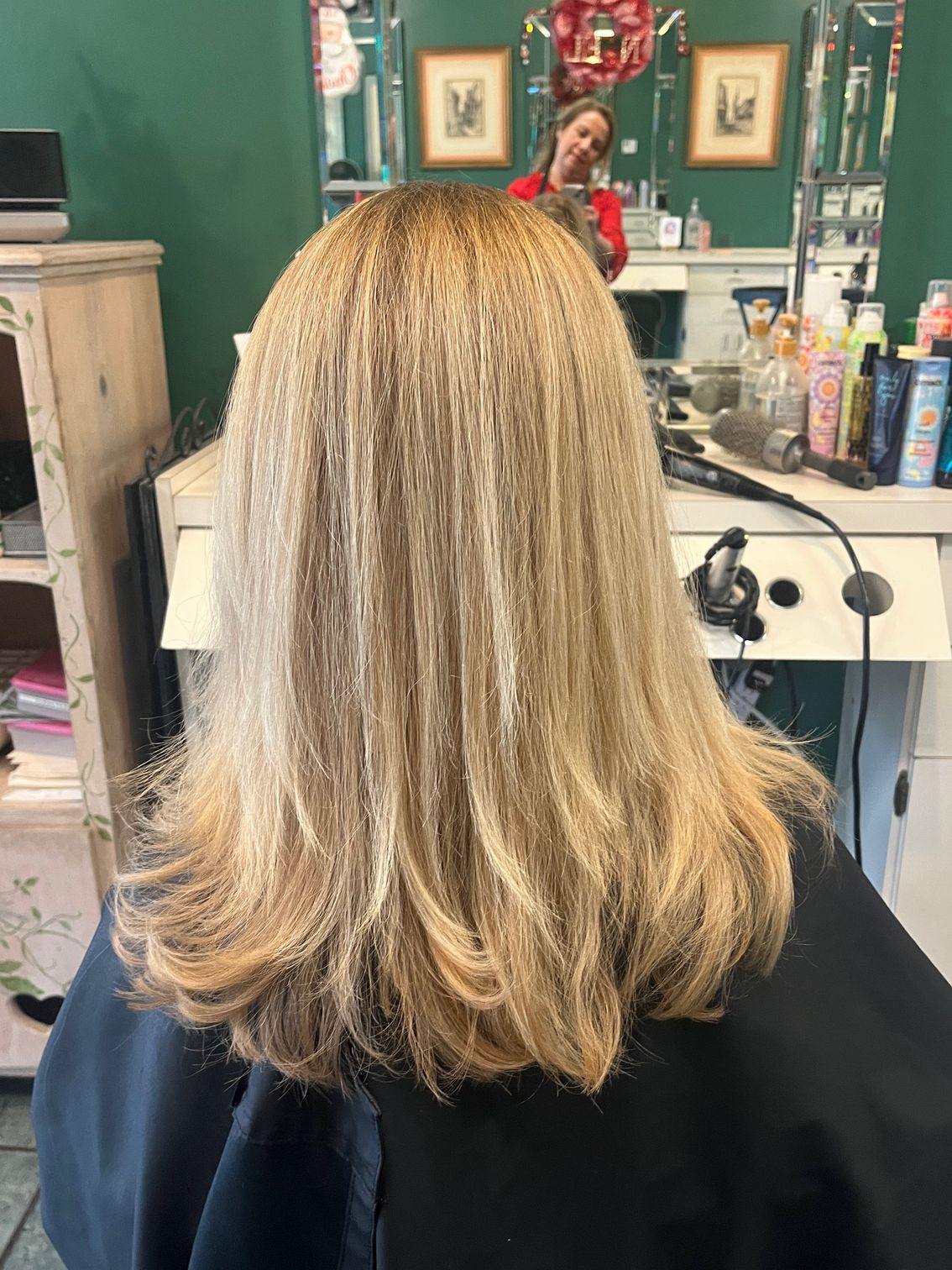 Woman with layered blonde hair sitting in a salon chair, facing away from the camera.
