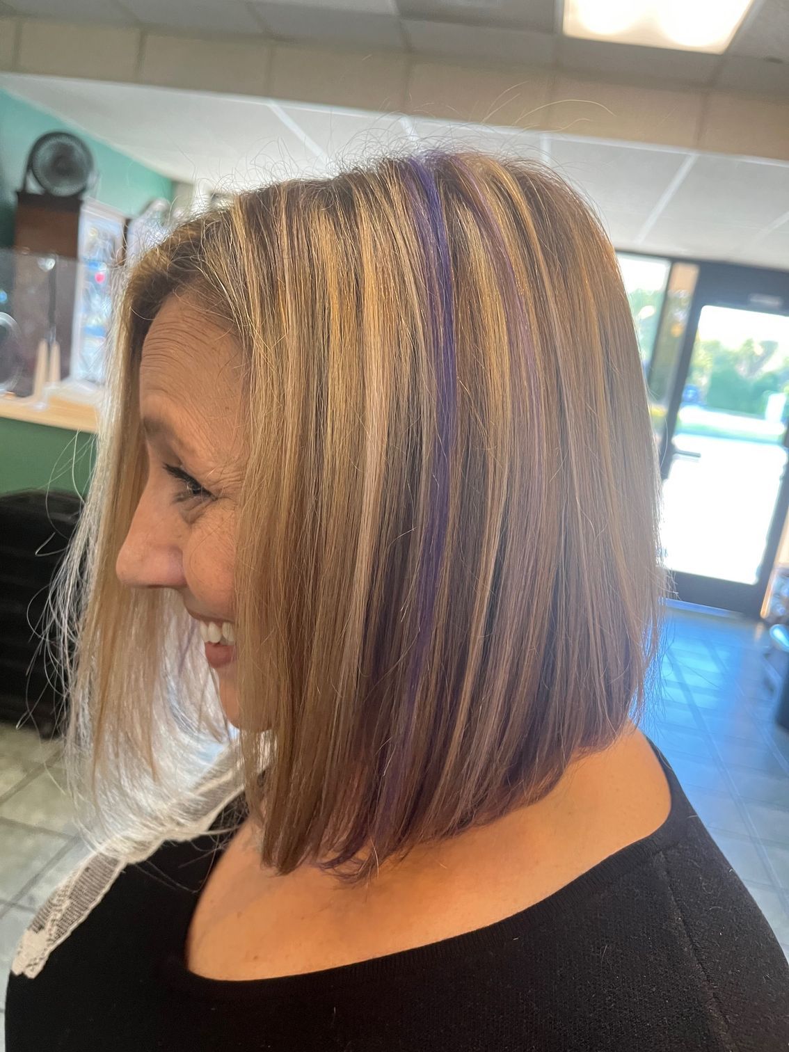 Woman with blonde and purple highlighted bob haircut smiling indoors.