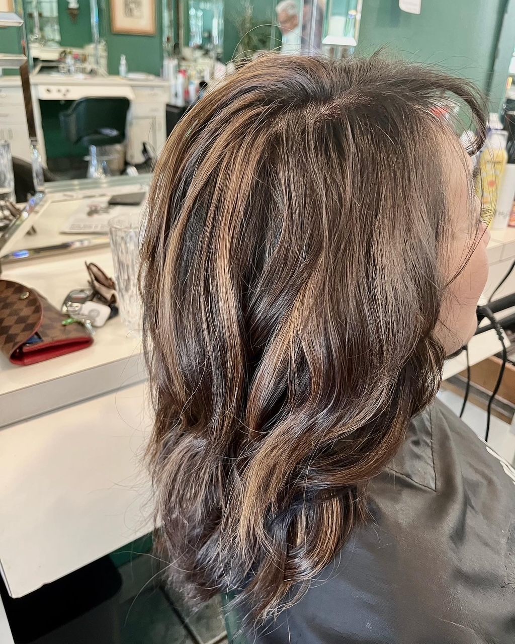 Woman's brown wavy hair with blonde highlights styled in a salon, a black cape on.