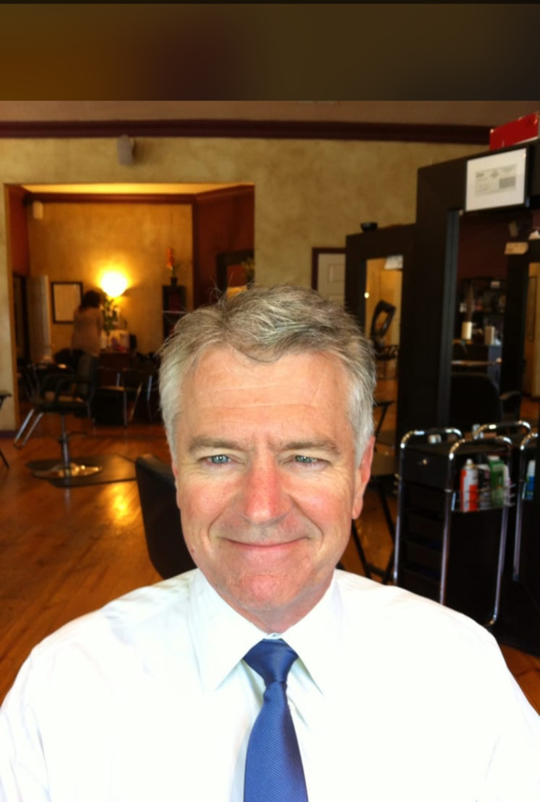 Man with gray hair wearing a white shirt and blue tie in a hair salon.