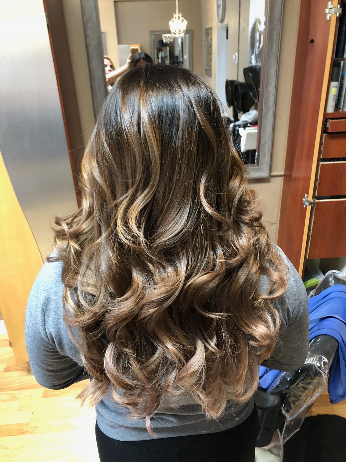 Woman with long, wavy brown hair with blonde highlights at a salon.