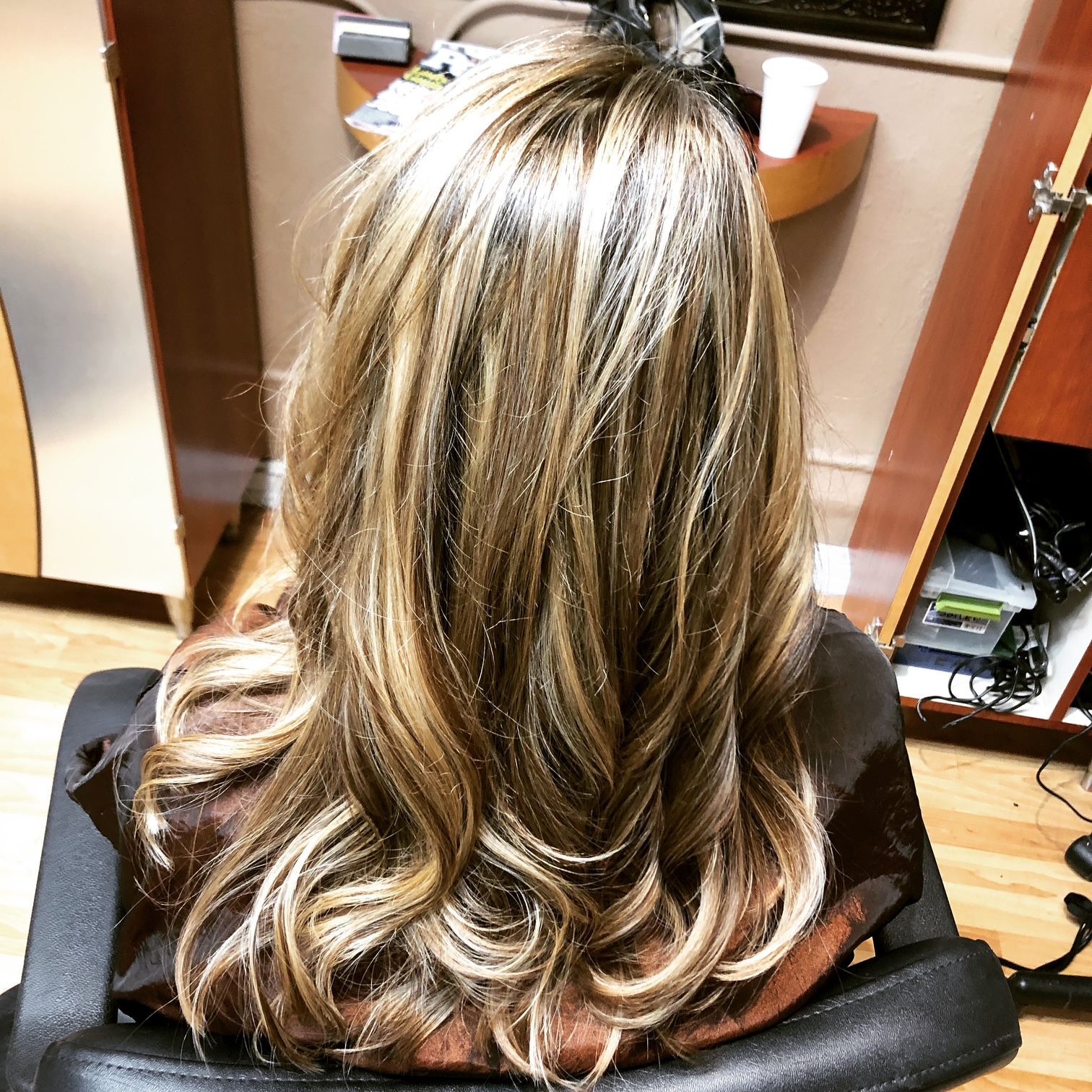 Woman with long wavy hair, highlighted with blonde and brown tones, styled at salon.