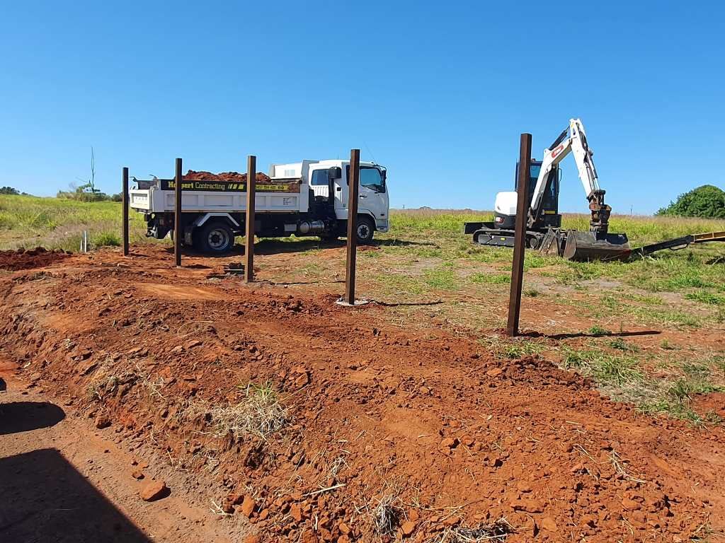 Construction Site with Wooden Posts Set in Red Dirt, Truck, Excavator — On The Mark Landscaping in Innes Park, QLD