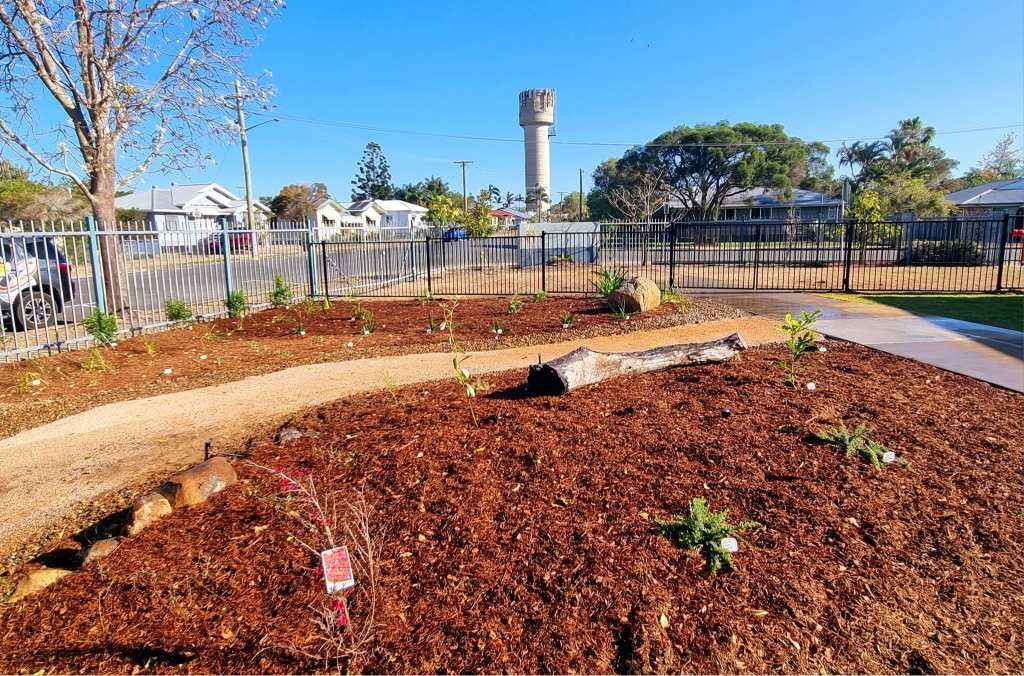Garden Bed With Mulch, Pathway, Log, Plants, Fence, and Water Tower — On The Mark Landscaping in Innes Park, QLD