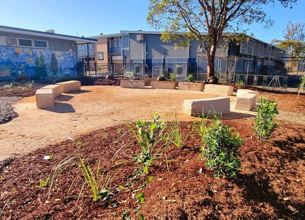 A Landscaped Outdoor Seating Area With Stone Benches, Tan Ground, and Plantings — On The Mark Landscaping in Bargara, QLD