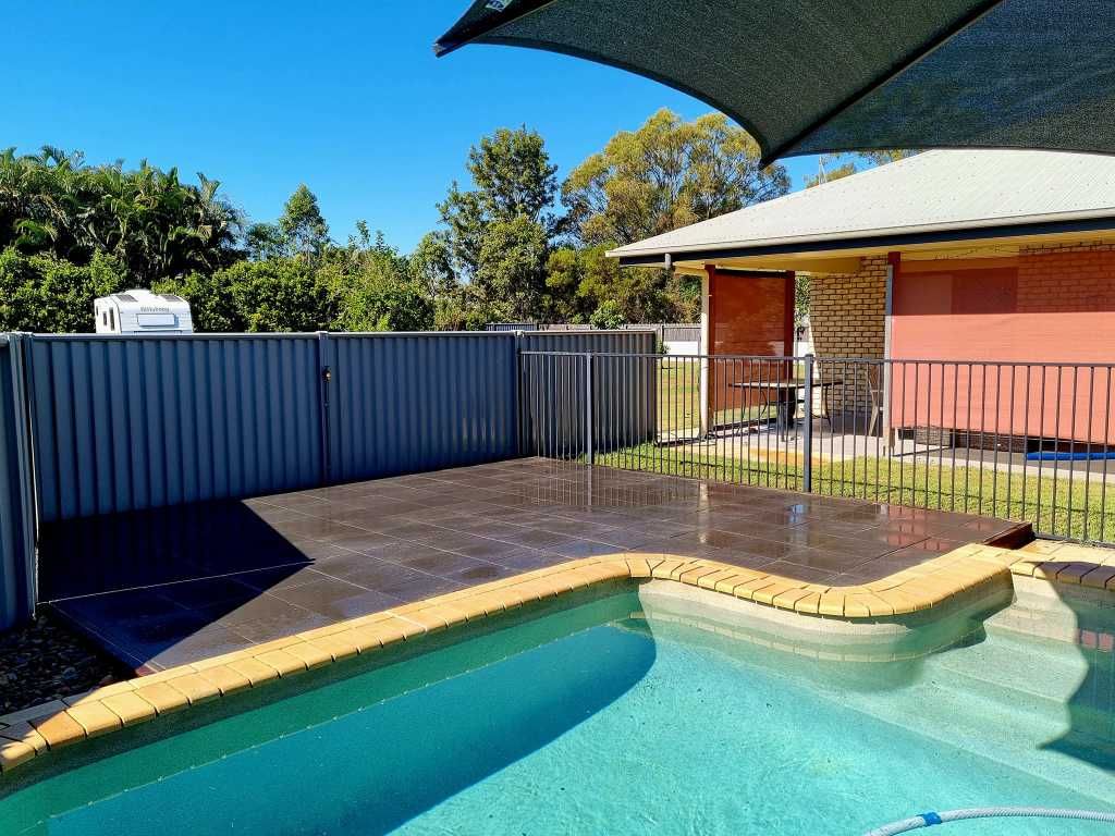 Pool Area With Blue Water, Brick Surround, Dark Grey Patio, Fence, and Shade — On The Mark Landscaping in Branyan, QLD