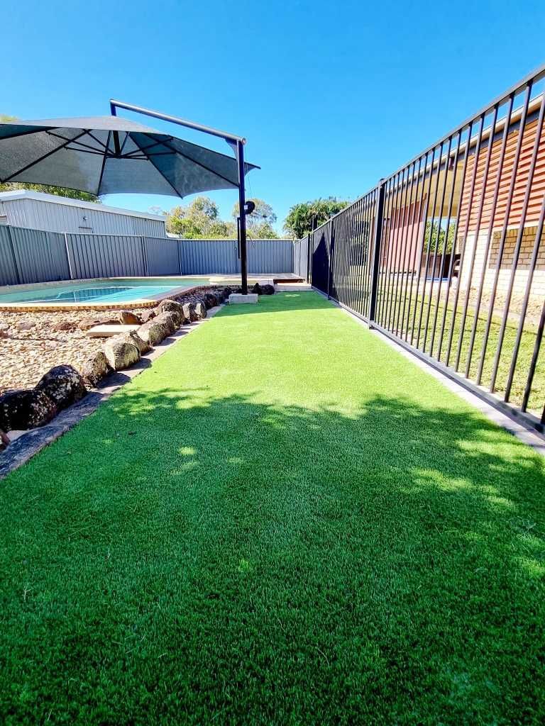 Green Artificial Turf in a Backyard With a Black Fence, Umbrella, and Pool — On The Mark Landscaping in Branyan, QLD