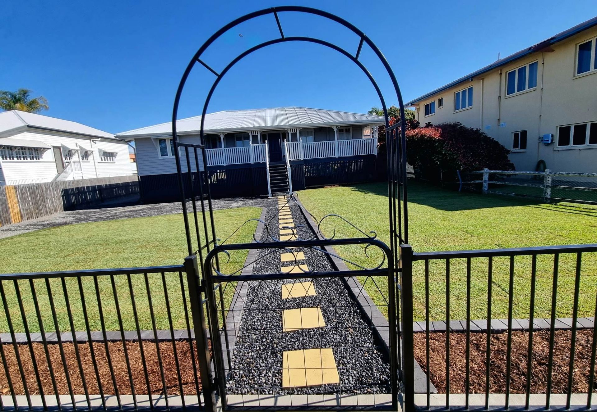 Metal Archway and Gate Lead to a House With a Stone Pathway and Lawn — On The Mark Landscaping in Branyan, QLD
