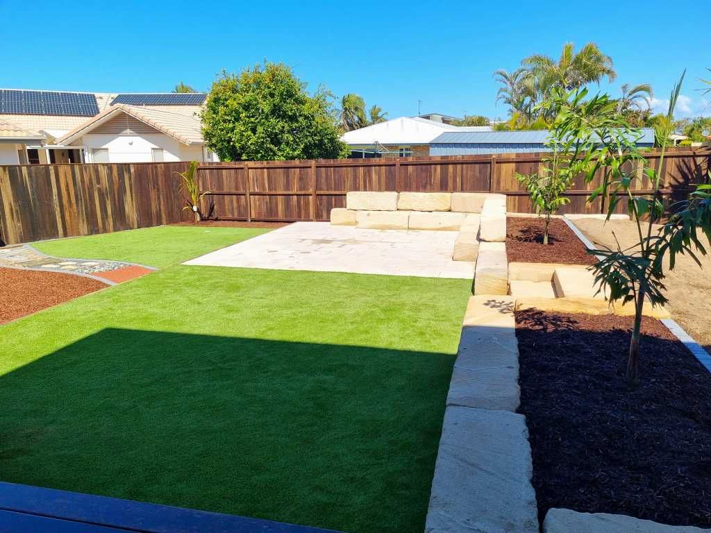 Backyard With Green Lawn, Wooden Fence, Stone Retaining Wall, Mulch, and Trees — On The Mark Landscaping in Branyan, QLD