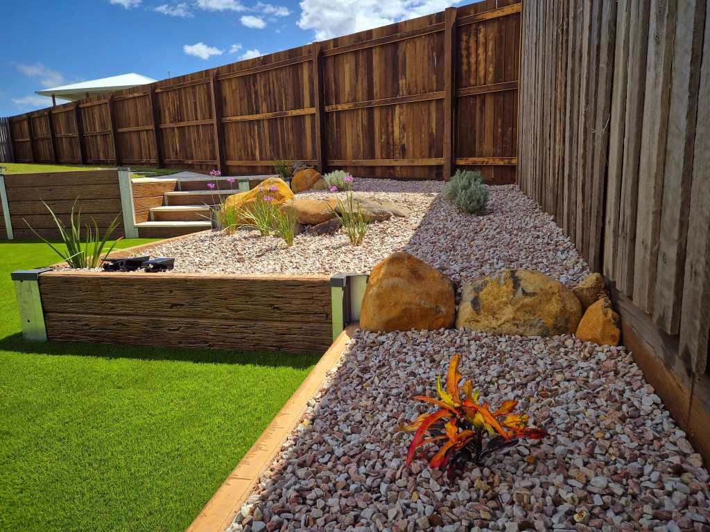Wooden Fence Borders a Gravel and Rock Landscaped Garden With a Retaining Wall — On The Mark Landscaping in Branyan, QLD