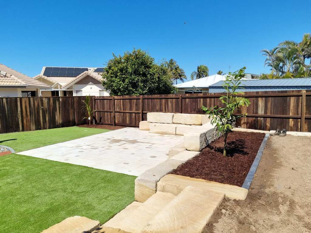 Backyard With Artificial Grass, Stone Patio, Wooden Fence, and a Young Tree — On The Mark Landscaping in Branyan, QLD