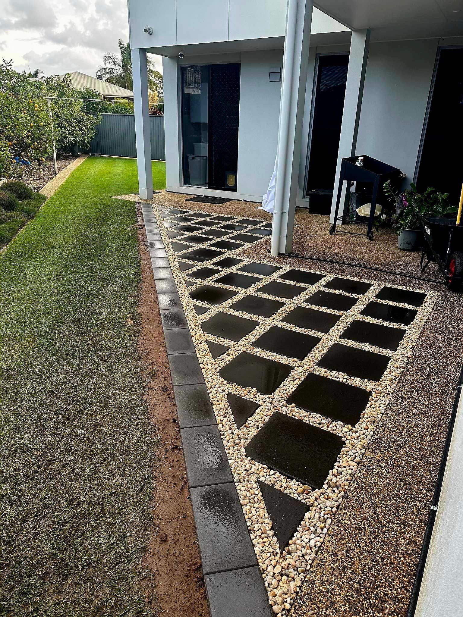 Patio With Black Square Tiles, Gravel, and Grass Next to a Modern Building — On The Mark Landscaping in Branyan, QLD
