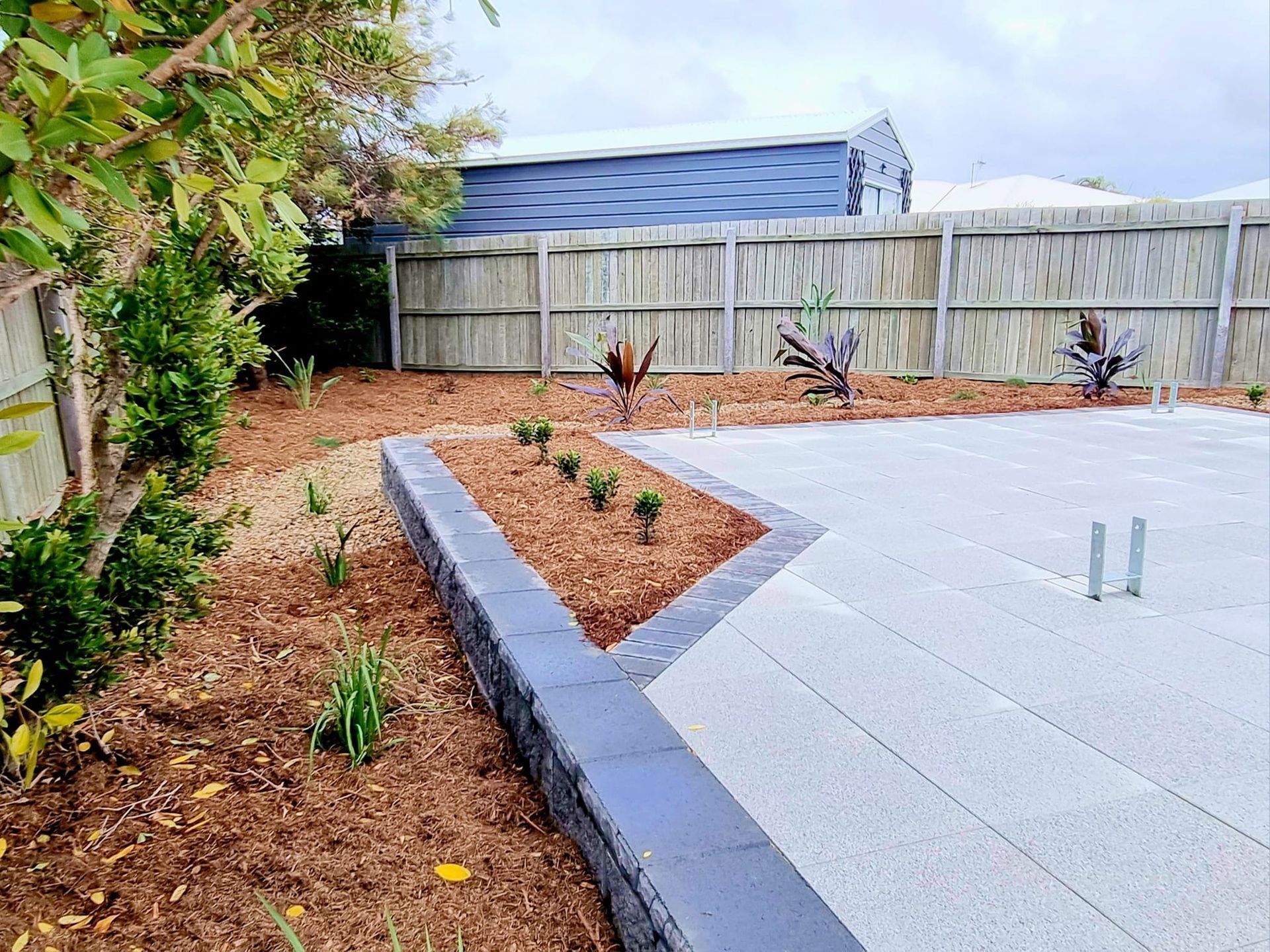 Backyard With Paved Area, Garden Bed With Plants, and Wooden Fence — On The Mark Landscaping in Branyan, QLD