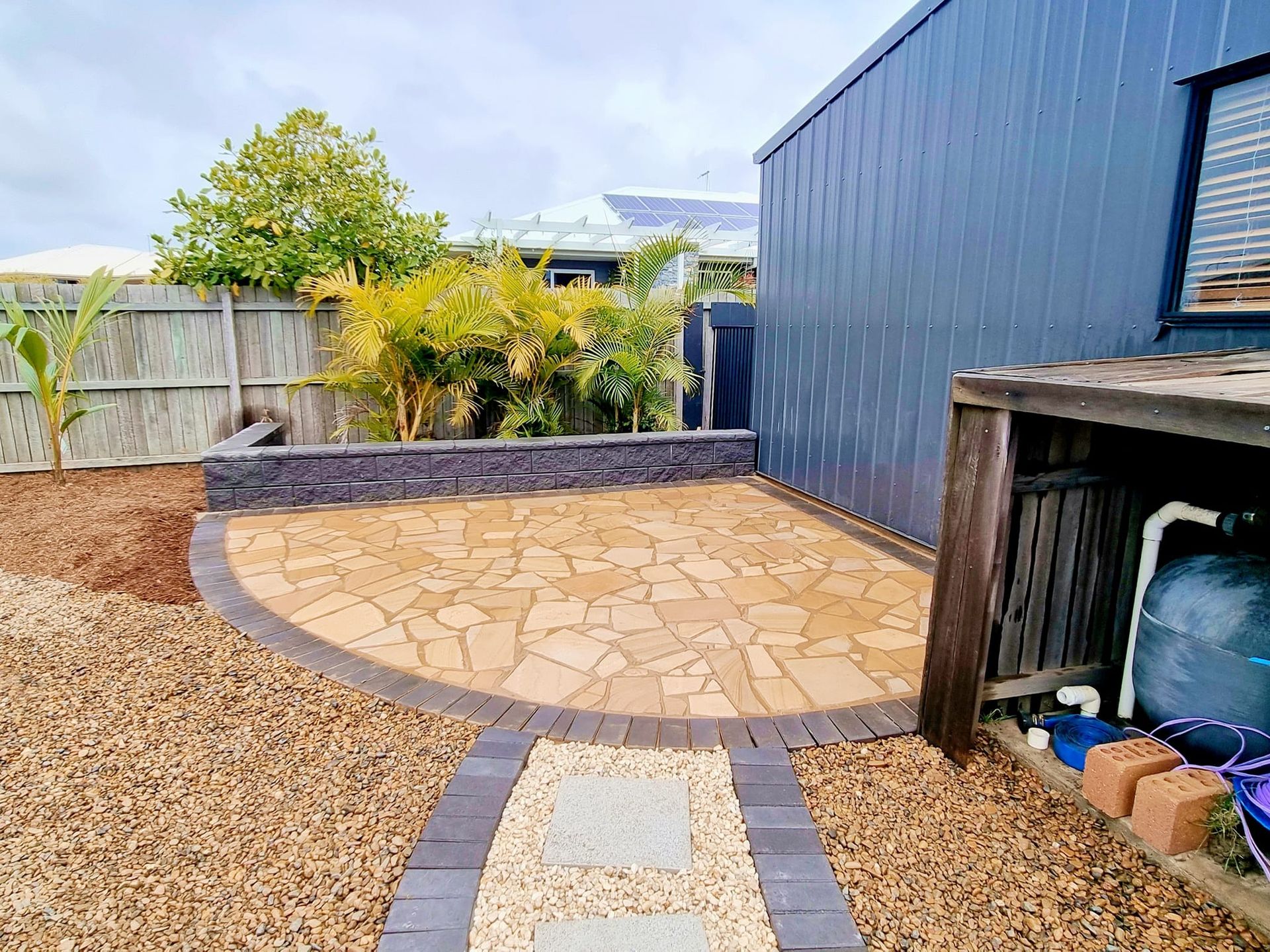 Stone Patio With Pathway, Brown Gravel, and Blue Shed Exterior — On The Mark Landscaping in Branyan, QLD