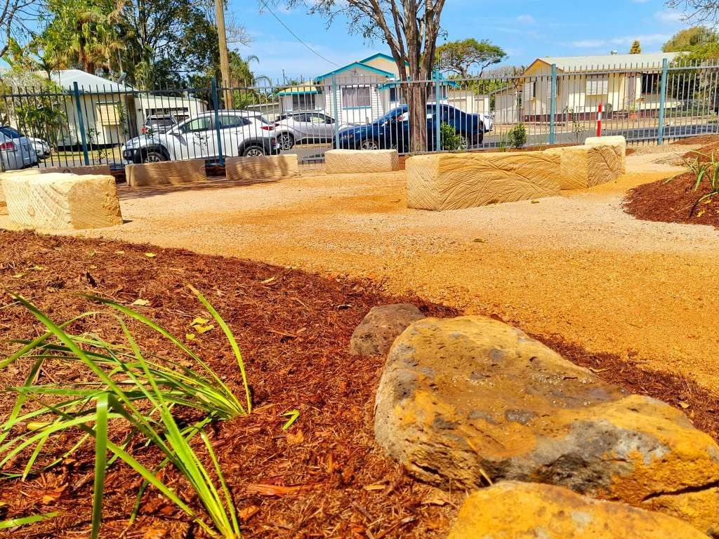 A Gravel Play Area With Large Rocks and Straw Seating in Front of a School — On The Mark Landscaping in Burnett Heads, QLD
