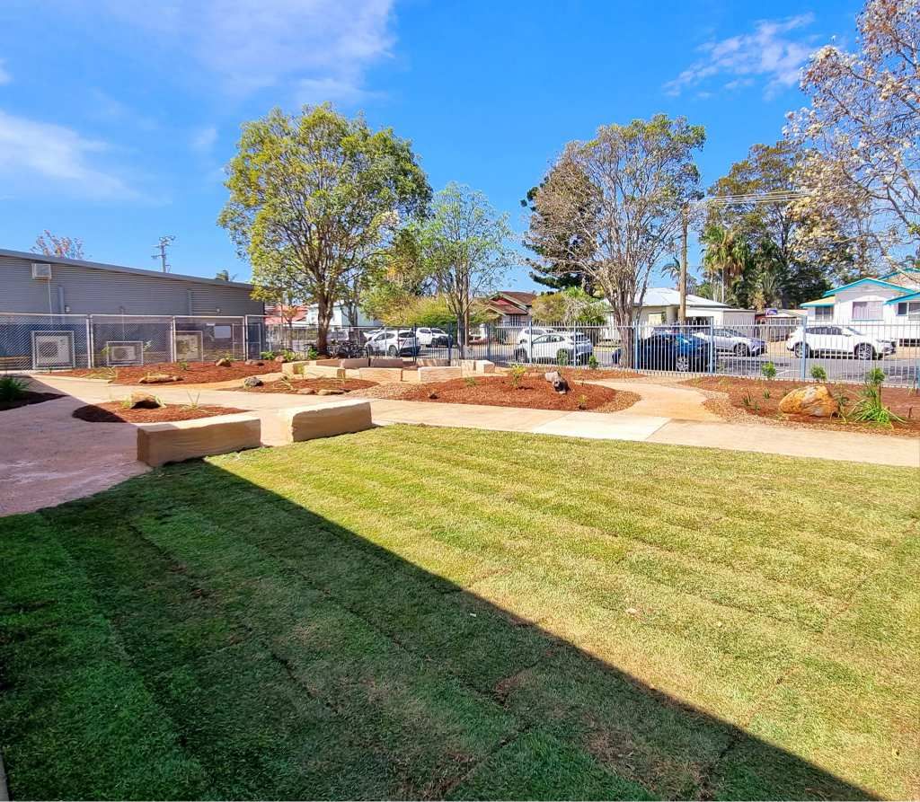 Green Lawn, Stone Benches, and Trees in an Outdoor Space With Cars and Buildings — On The Mark Landscaping in Branyan, QLD