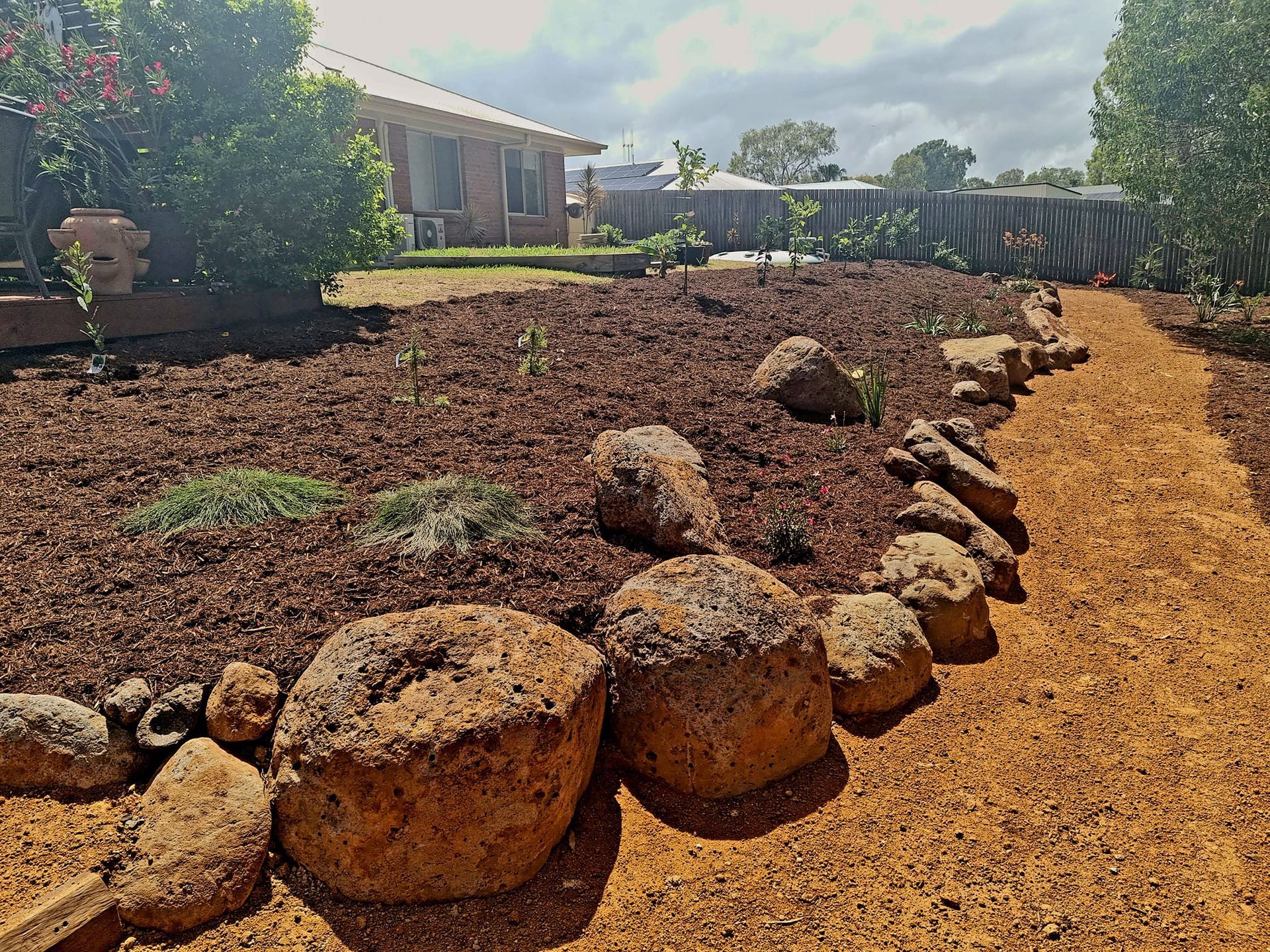 A Backyard Garden With a Stone Path, Brown Mulch, and a House in the Background — On The Mark Landscaping in Branyan, QLD