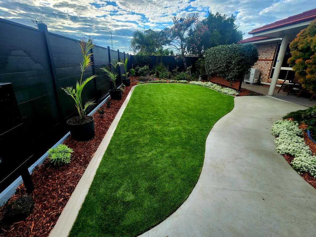 Lawn in a Backyard With a Curved Concrete Path, Garden Beds and a Black Fence — On The Mark Landscaping in Branyan, QLD