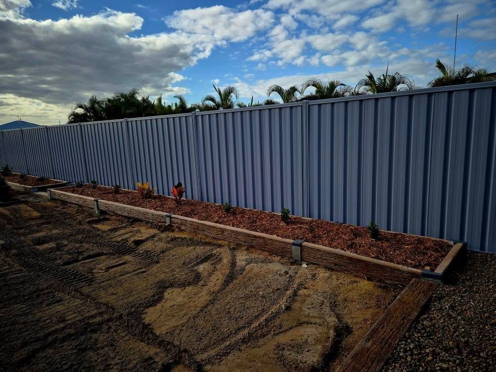 A Long Metal Fence With a Garden Bed Filled With Mulch and Plants — On The Mark Landscaping in Branyan, QLD