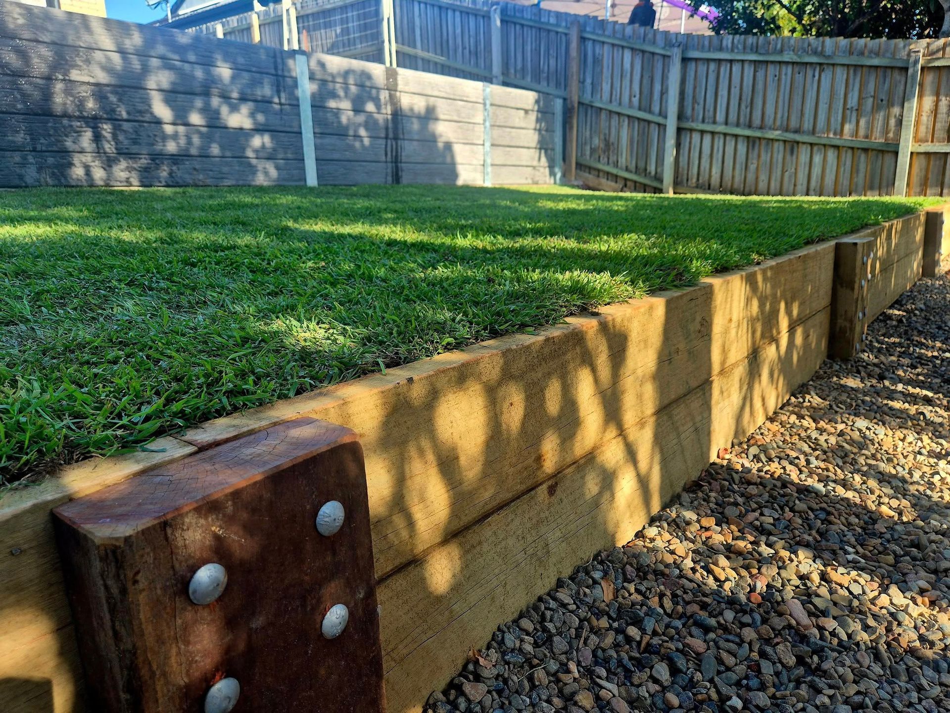 Wooden Retaining Wall Holding Back a Patch of Green Grass — On The Mark Landscaping in Branyan, QLD