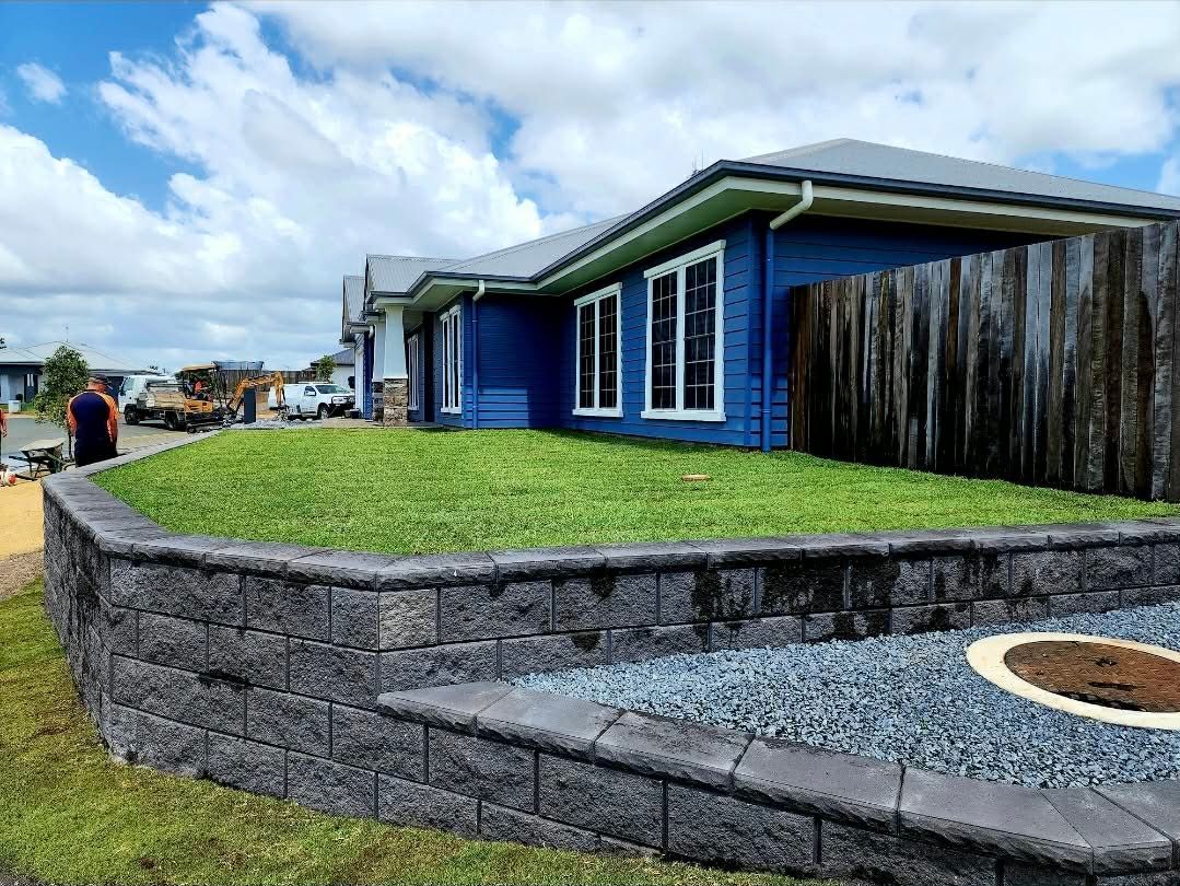 Blue House With Retaining Wall, Green Grass, and Blue Sky — On The Mark Landscaping in Branyan, QLD