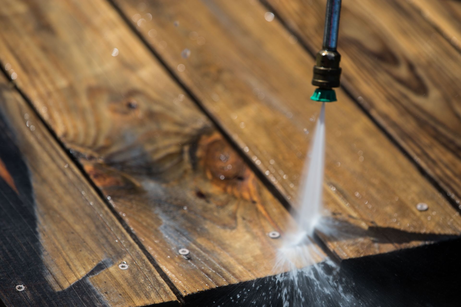 A person is using a high pressure washer to clean a wooden deck.