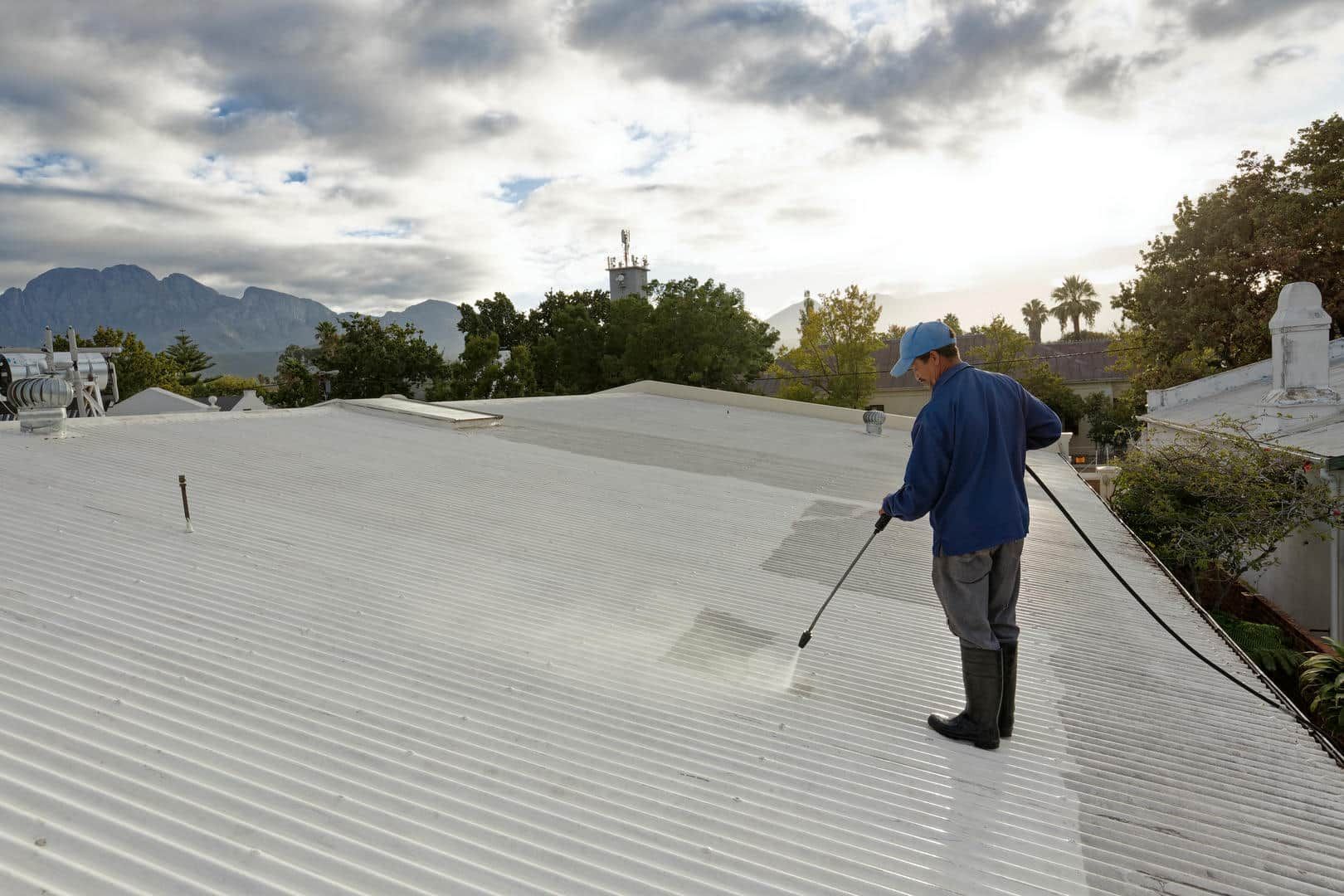 A man is spraying a white roof with a hose.