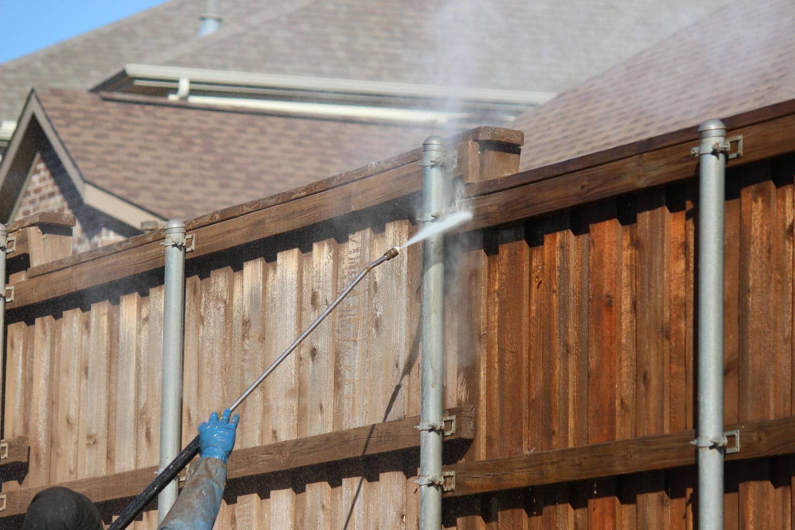 A man is cleaning a wooden fence with a high pressure washer.