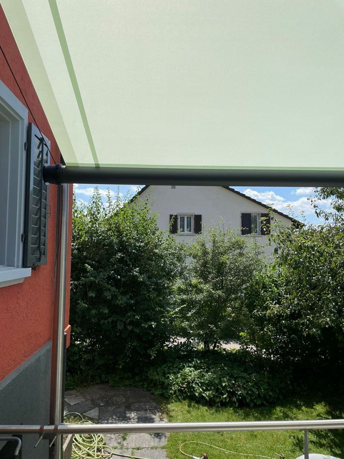 An der Seite eines roten Hauses hängt eine grüne Markise.