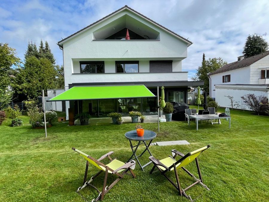 Ein Haus mit einer grünen Markise und Stühlen davor.