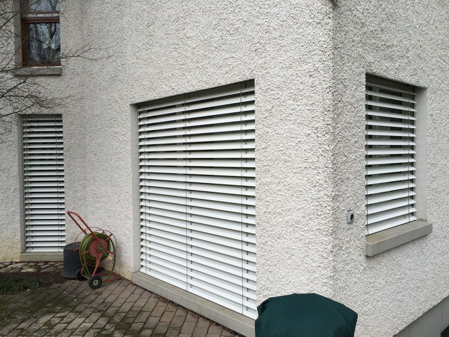 Ein weisses Gebäude mit weissen Jalousien an den Fenstern.