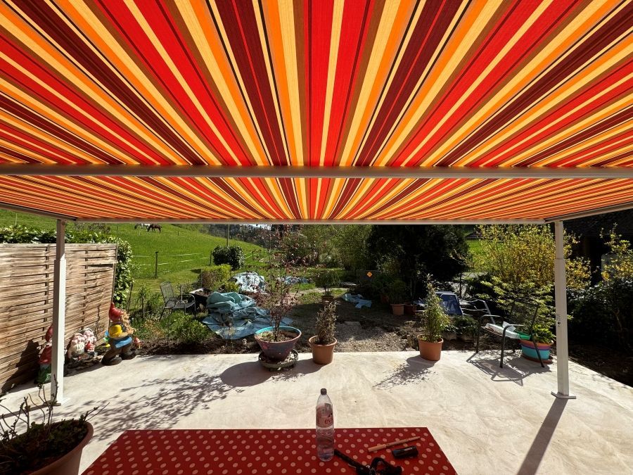 Eine Terrasse mit einer rot-gelb gestreiften Markise darüber